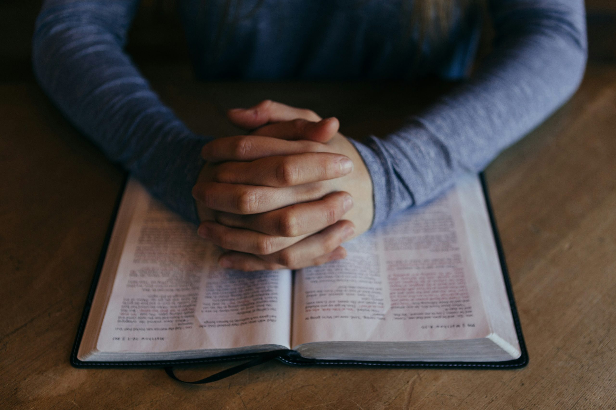 A person with clasped hands over an open Bible.