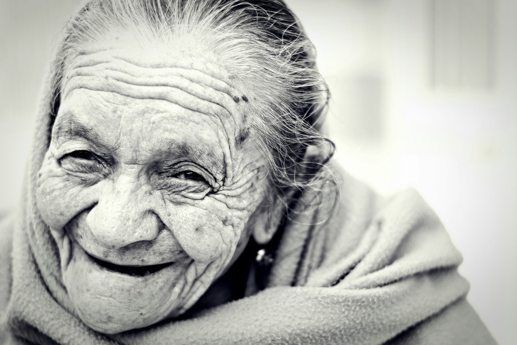 An old woman, like Naomi in the Bible, with a face covered with wrinkles laughs into the camera, showing her journey from heartbreak to joy