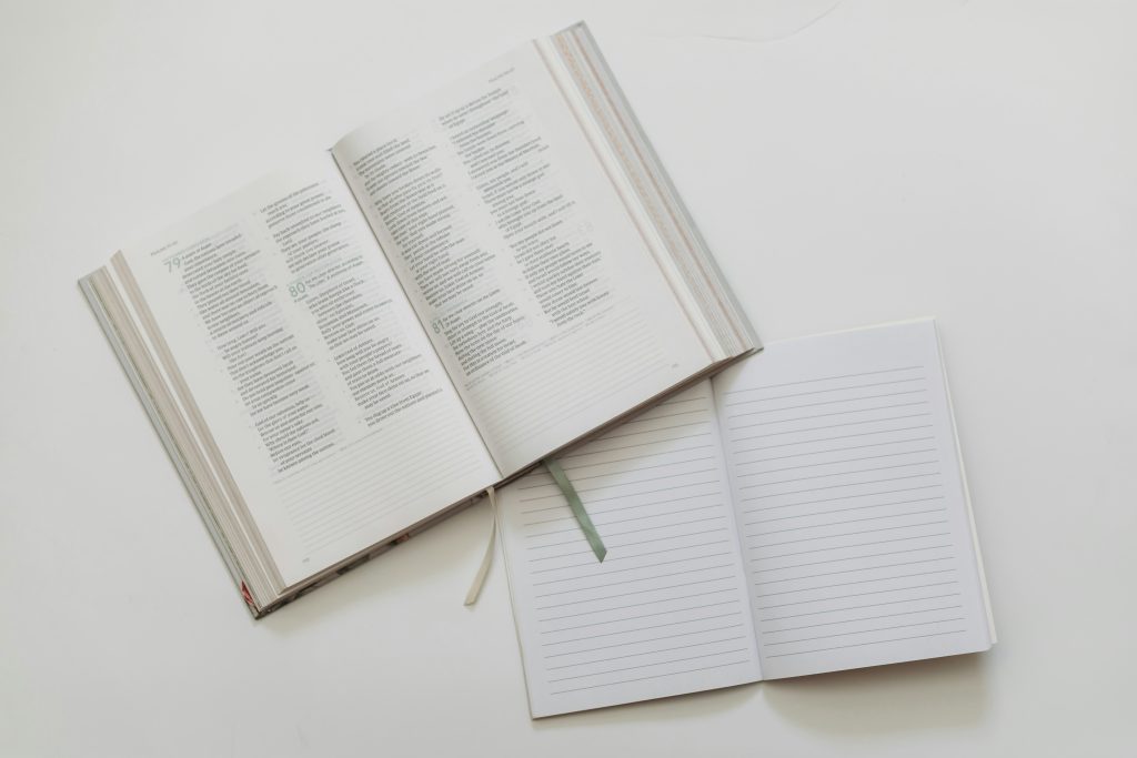 Um livro aberto fica ao lado de um caderno pautado em uma superfície branca, ecoando a paz encontrada nas páginas de um edredom na Bíblia.