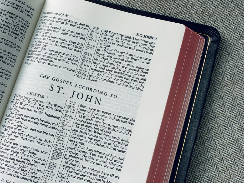 Uma Bíblia aberta repousa sobre uma superfície cinza texturizada, revelando o início do Evangelho de João e sua profunda introdução ao Consolador na Bíblia.