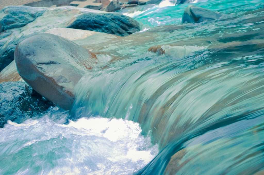 Flowing turquoise river cascading over smooth rocks, creating white water ripples and waves, showing gentleness
