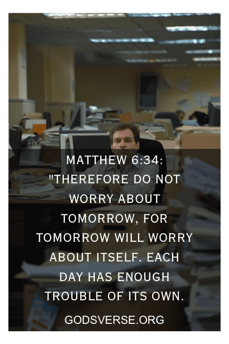 Person sitting at a cluttered office desk, with a Bible verse overlay: "Matthew 6:34" and website URL "GODSVERSE.ORG." Visit GODSVERSE.ORG for more Bible verses for stress at work.