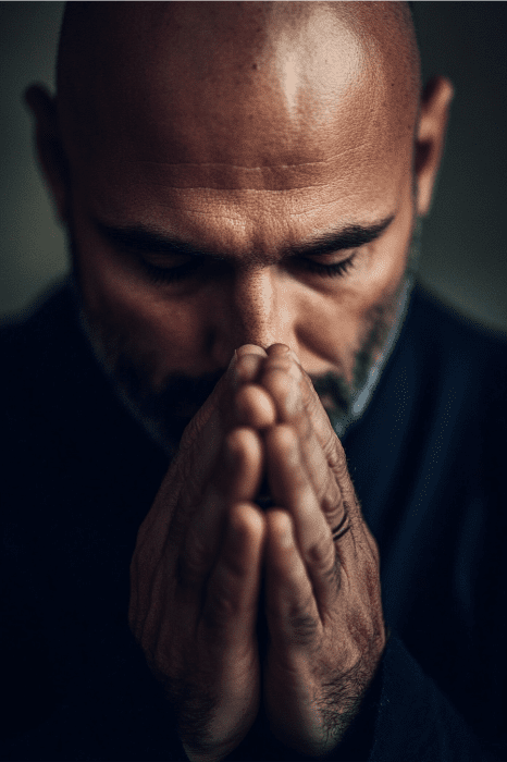 Un hombre calvo con los ojos cerrados mantiene las manos en posición de oración contra la cara, reflexionando en oraciones por su familia de la iglesia y con aspecto contemplativo.