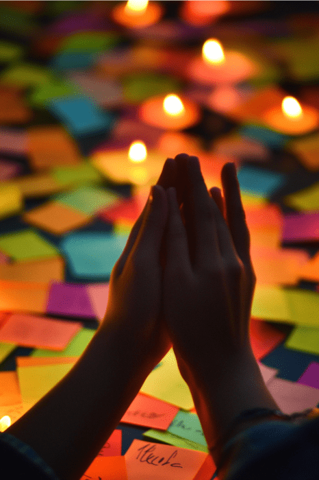 Mãos em oração sobre notas adesivas coloridas, criando uma cena inspiradora para a Escola Dominical. As velas acrescentam uma atmosfera calorosa e brilhante, perfeita para participar de jogos de oração.