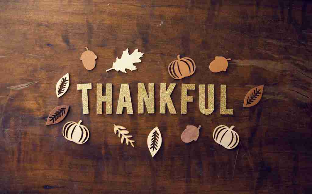 The word "Thankful," accompanied by autumn leaves and pumpkins on a wooden background, sets the perfect scene for thanksgiving lessons for children's church.