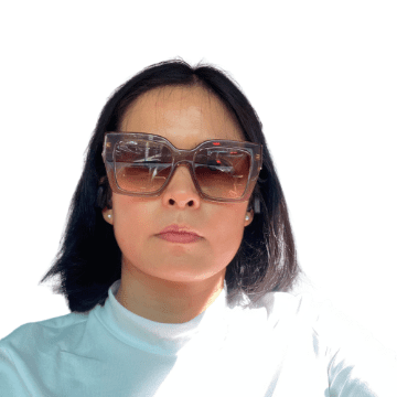 Person with short hair wearing large sunglasses and a white shirt against a plain background.