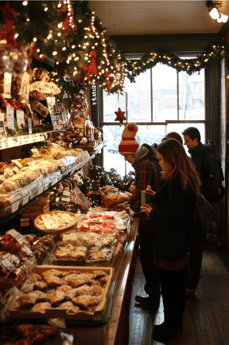 As pessoas procuram produtos de padaria em uma loja aconchegante e decorada, com luzes de Natal e uma vista de neve do lado de fora da janela, lembrando os eventos da igreja que promovem o calor e o espírito comunitário.
