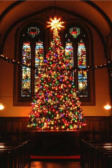 A brightly lit Christmas tree inside a church casts a warm glow, complementing the stained glass windows, setting the perfect backdrop for innovative Christmas Sermon Series ideas.