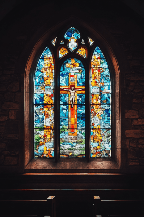 O vitral da igreja, repleto de tons vibrantes de azul, laranja e amarelo, representando uma cena de crucifixo, serve como um belo pano de fundo para as ideias da série de sermões de Páscoa.