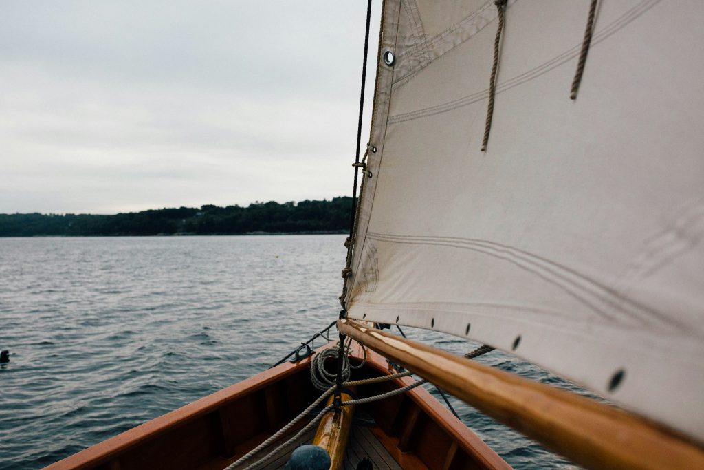 View from a sailboat's bow, accompanied by the sail gracefully cutting through open water under a cloudy sky, almost like nature's grand prophecy.