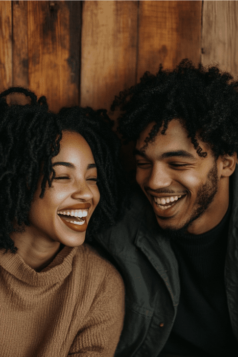 A smiling couple looks at each other, seated against a wooden background, as if recalling the enduring love found in the story of Rebekah in the Bible.