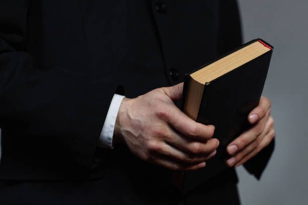 Dressed in a black suit, the person clutches a closed book with a mysterious air, its cover black and page edges tinted red, perhaps contemplating the profound question: What are the 73 Books in the Bible?.