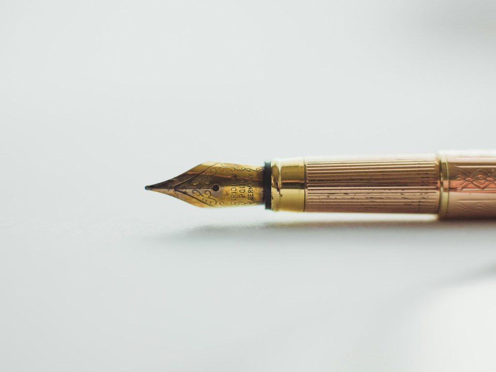 Uma caneta-tinteiro com ponta dourada e detalhes ornamentados está sobre um fundo branco, lembrando a elegância que pode ter sido usada para escrever textos antigos como Atos na Bíblia.