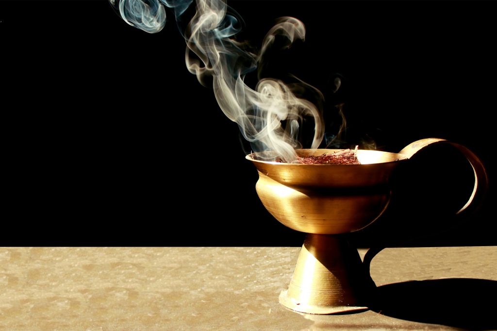 A brass incense burner, reminiscent of rituals mentioned in the Bible, emits swirling smoke against a dark background.