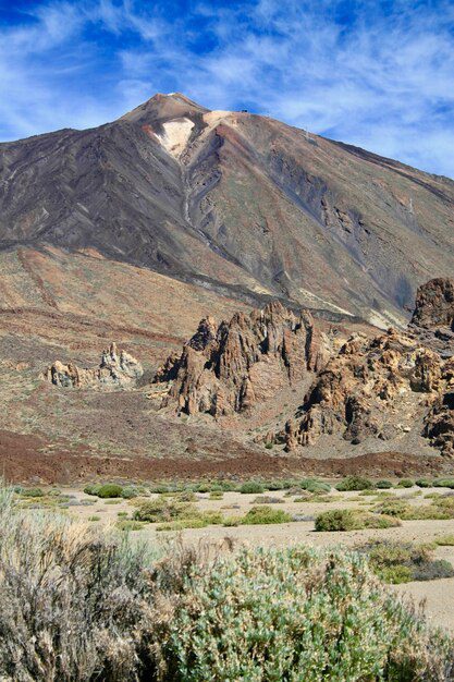 The rugged peaks of this mountain landscape resemble the legendary Mount Ararat from the Bible, with its sparse vegetation and a blue sky adorned by wispy clouds.