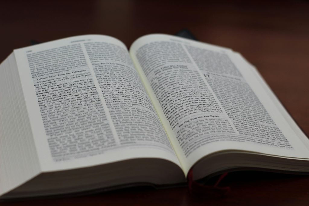 Um livro aberto com um texto que lembra os Filhos do Trovão da Bíblia adorna uma superfície branca. Uma delicada flor branca repousa sobre a página esquerda, acrescentando um toque de serenidade à cena.