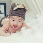 Jessica in the Bible: Meaning and Origin of the Name Smiling baby in a knitted hat and diaper lying on soft white fur near a "Bonjour" sign.
