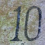 The number 10, often symbolizing divine order in the Bible, is painted in black on a weathered, moss-covered stone surface.