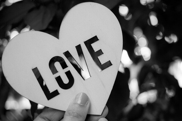 A hand holds a heart-shaped cutout with the word "LOVE," echoing the timeless love stories in the Bible, set against a blurred outdoor background.