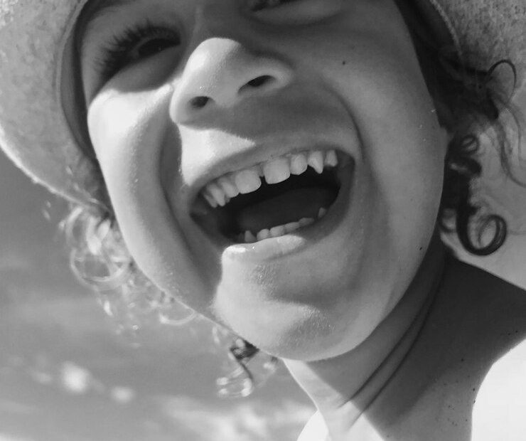 A child wearing a sunhat laughs joyfully outdoors, with the sky in the background, echoing the spirit of laughter in the Bible.