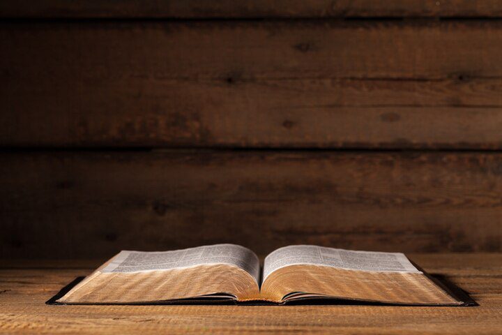 An open book with gold-edged pages rests on a wooden table against a wooden background, inviting reflection on what the Bible says about missions.