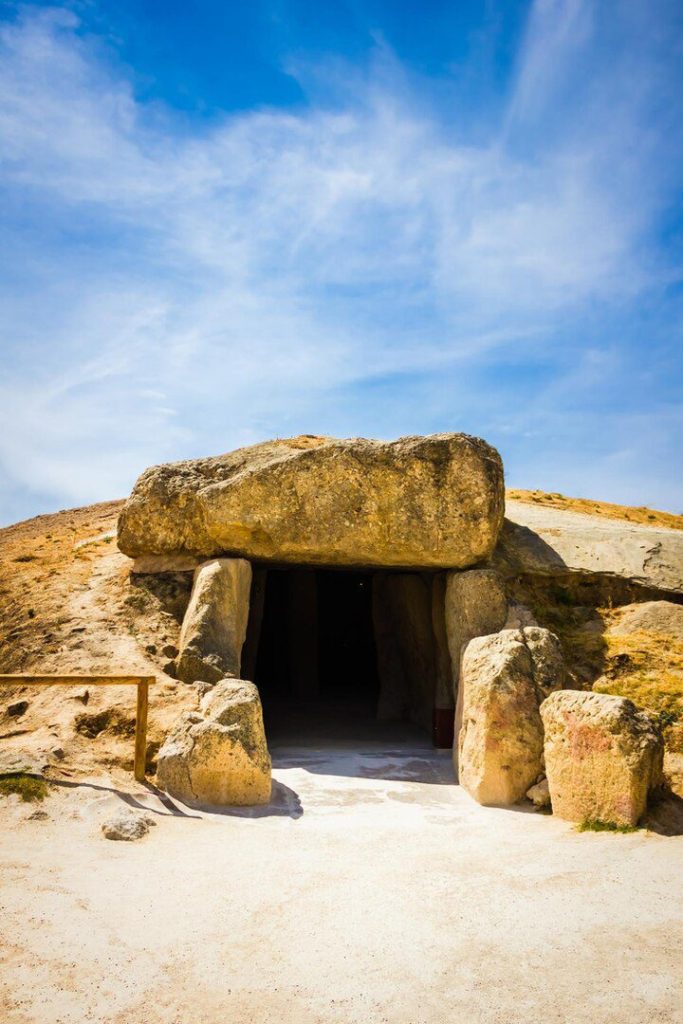 Ancient stone dolmen entrance under a blue sky, with large rocks forming a doorway into a mound—evoking the mysterious aura of sites mentioned alongside Legion in the Bible.